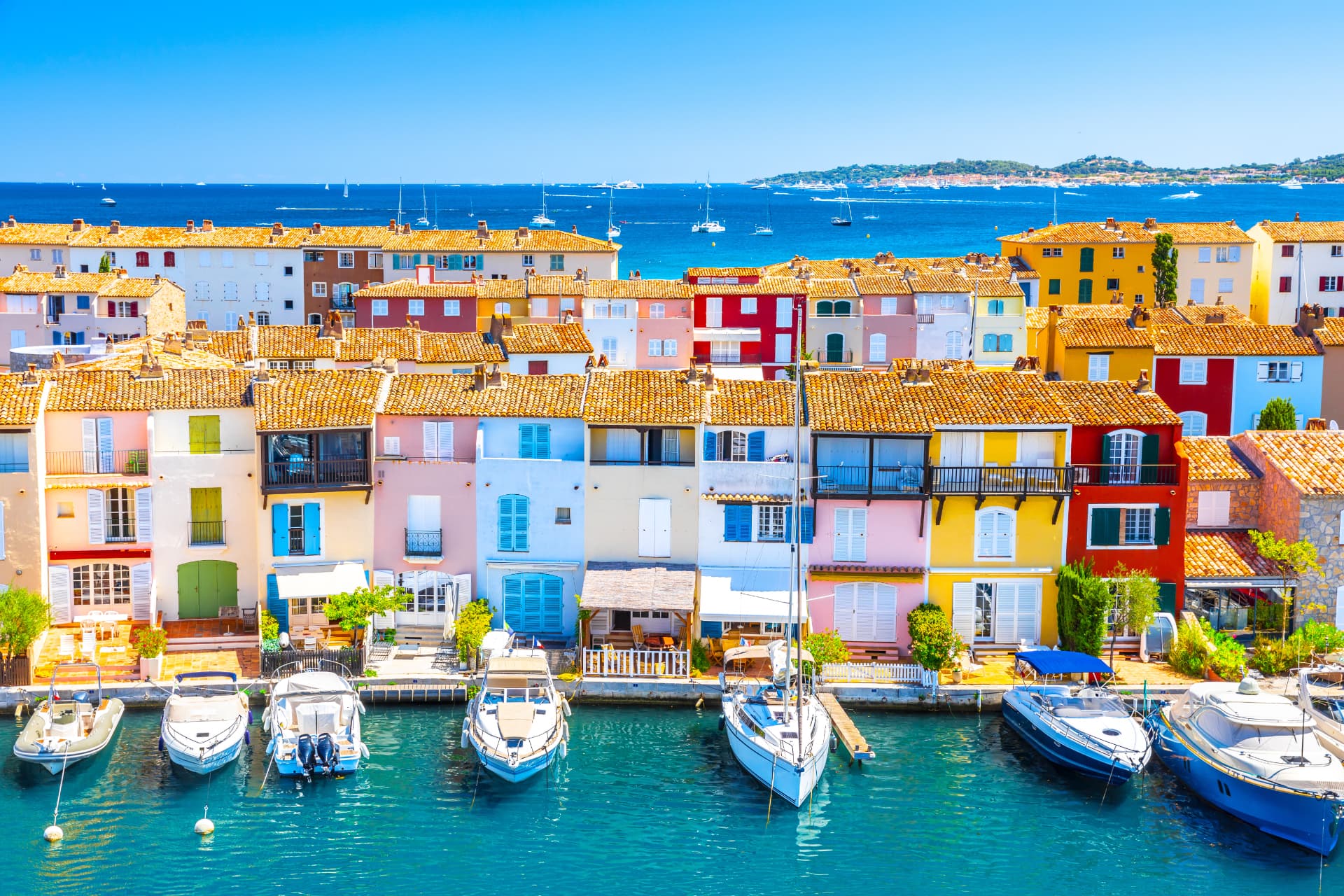 Maisons colorées de Port Grimaud au bord d'un canal, bateaux amarrés et Méditerranée en arrière-plan