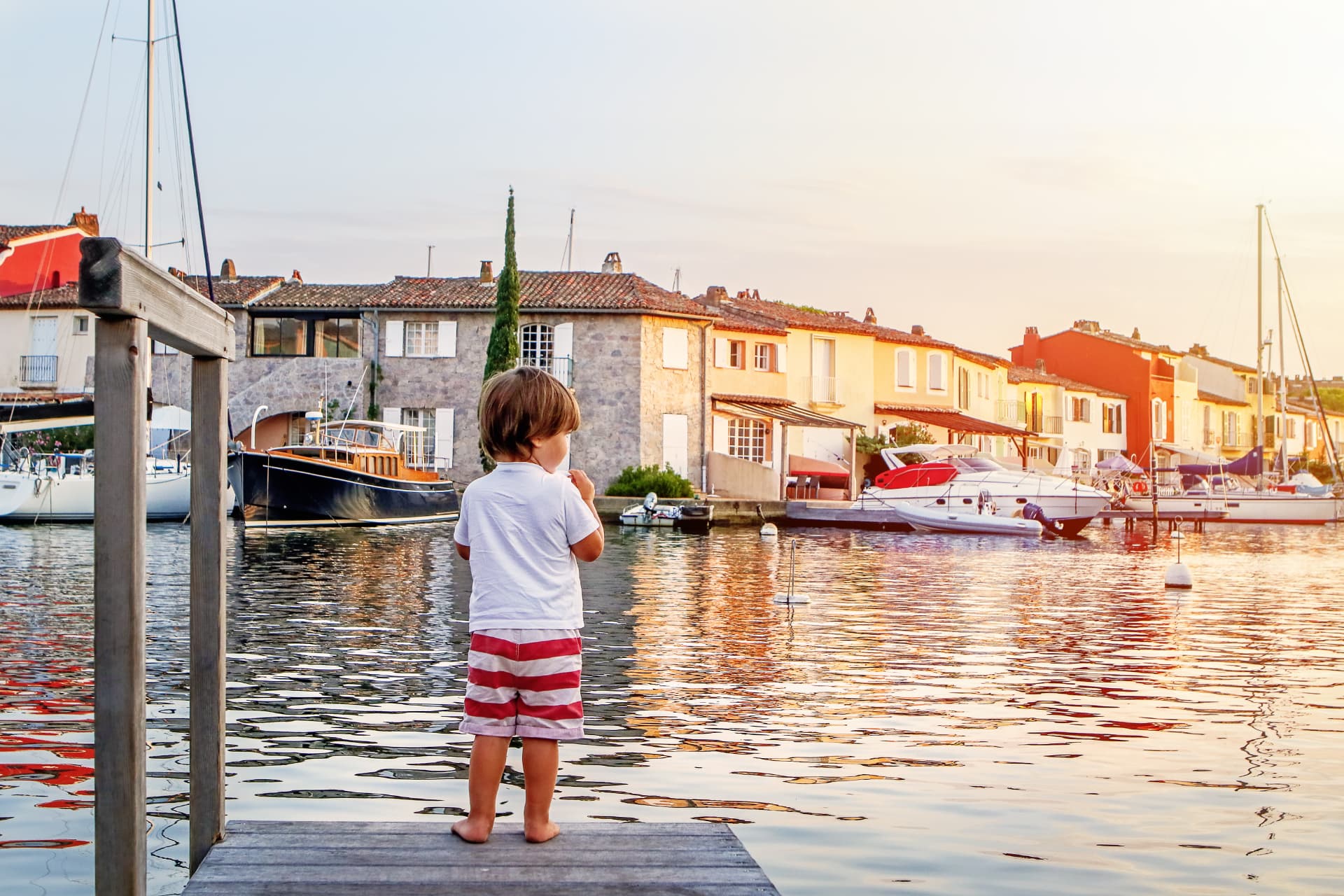 Enfant sur un ponton à Port Grimaud, face aux maisons colorées et aux bateaux des canaux